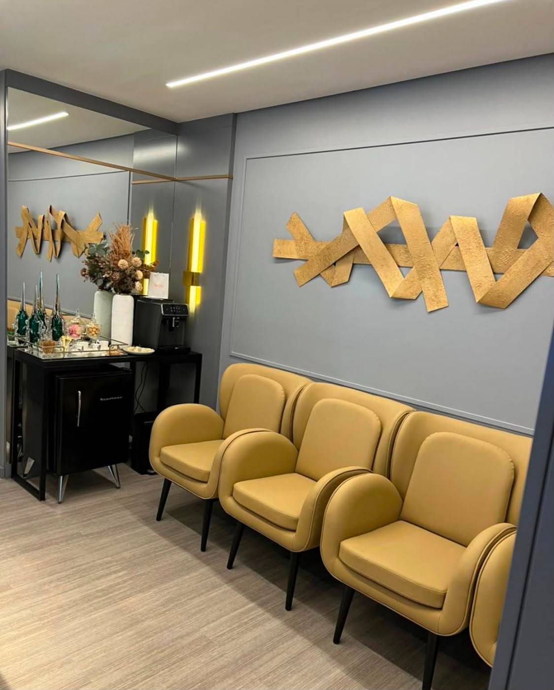Sala de espera do consultório: três poltronas mostarda diante de uma parede cinza com escultura dourada